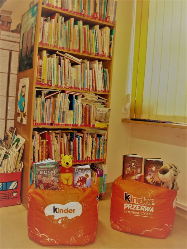 Zdjęcie przedstawia wypożyczalnię Bibliotek,i w której stoją dwie pufy z napisem Kinder Przerwa na wspólne czytanie oraz ułożone na nich książki.
