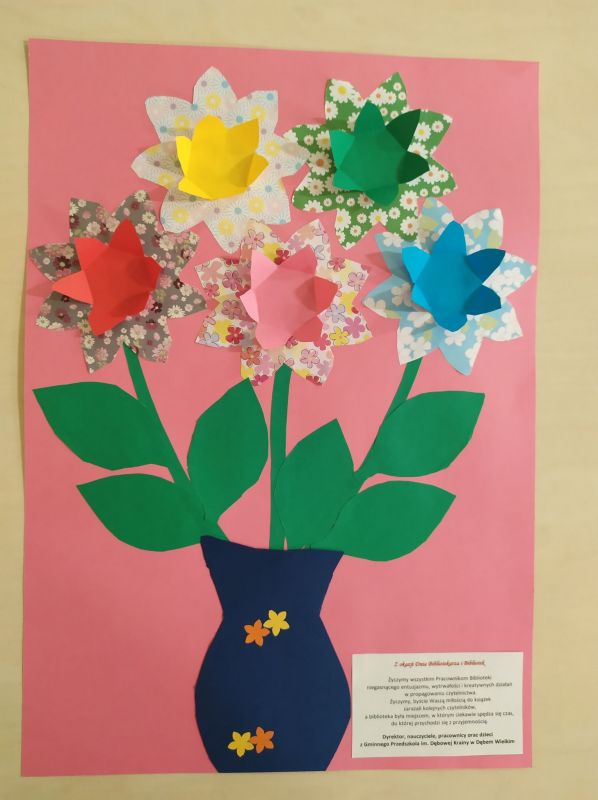 Zdjęcie przedstawia  wazon z kwiatami oraz życzenia od przedszkolaków z okazji Dnia Bibliotekarza i Bibliotek